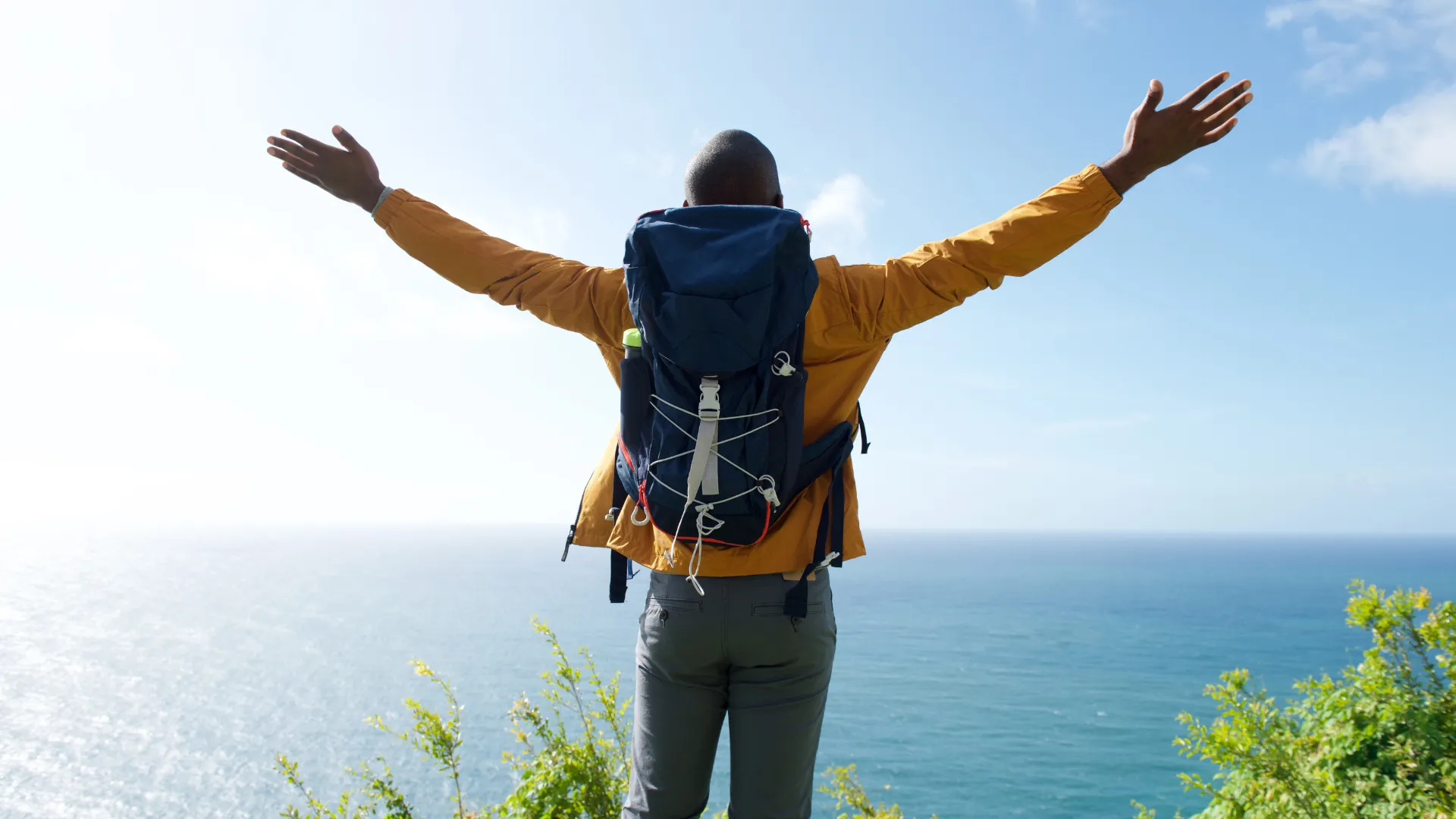 Person standing with arms raised while overlooking the water